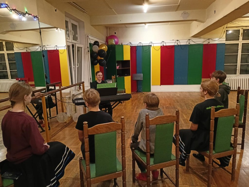 Zdjęcie z warsztatów w siedzibie Zespołu z dnia 30.11.2024. Dzieci siedzą na sali w trakcie zajęć ze śpiewu