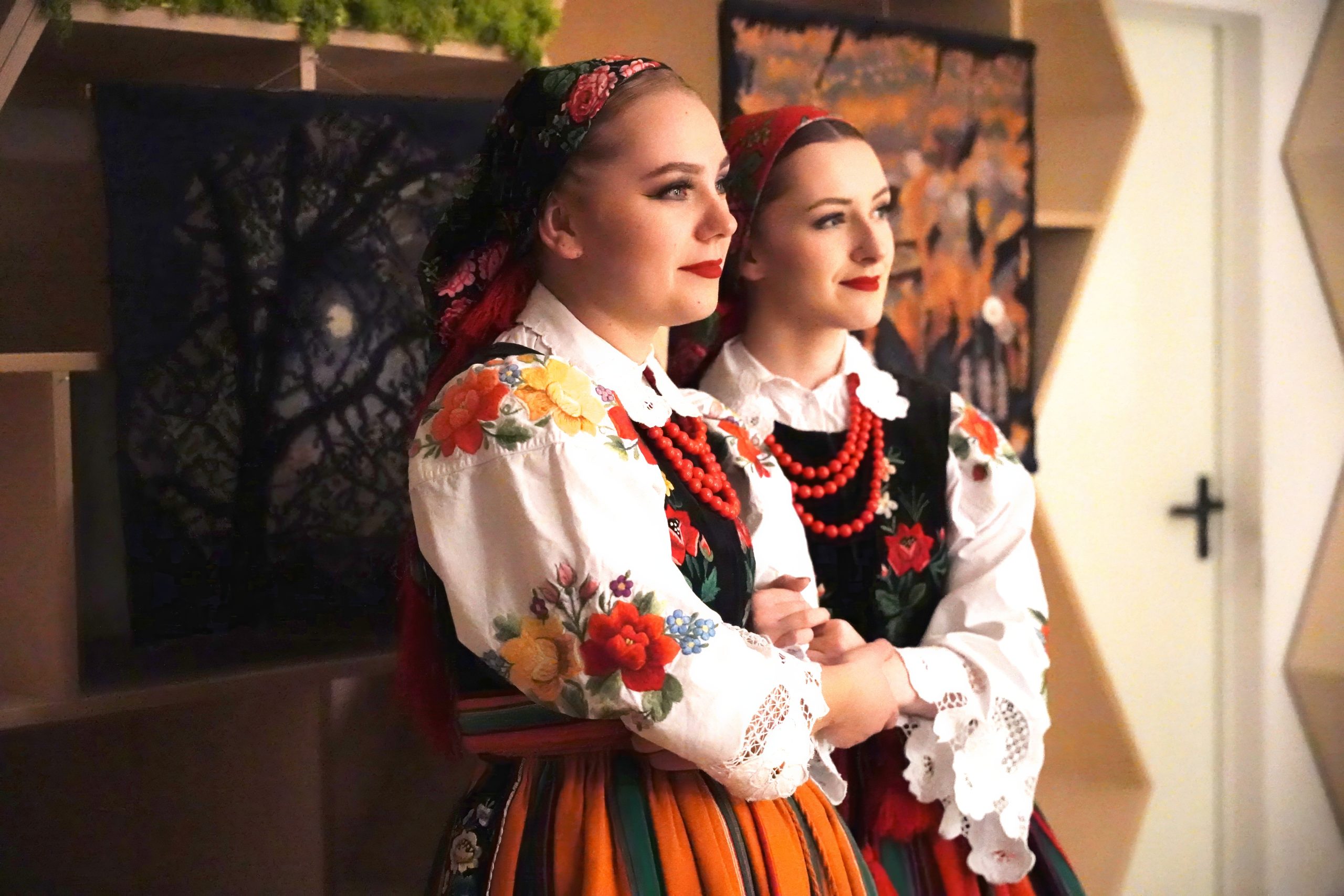 dziewczyny w strojach łowickich na tle obrazów patrzą w dal