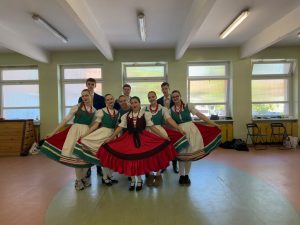 Młodzież w strojach dolnośląskich i dziewczynka w stroju polki warszawskiej pozuje do zdjęcia grupowego