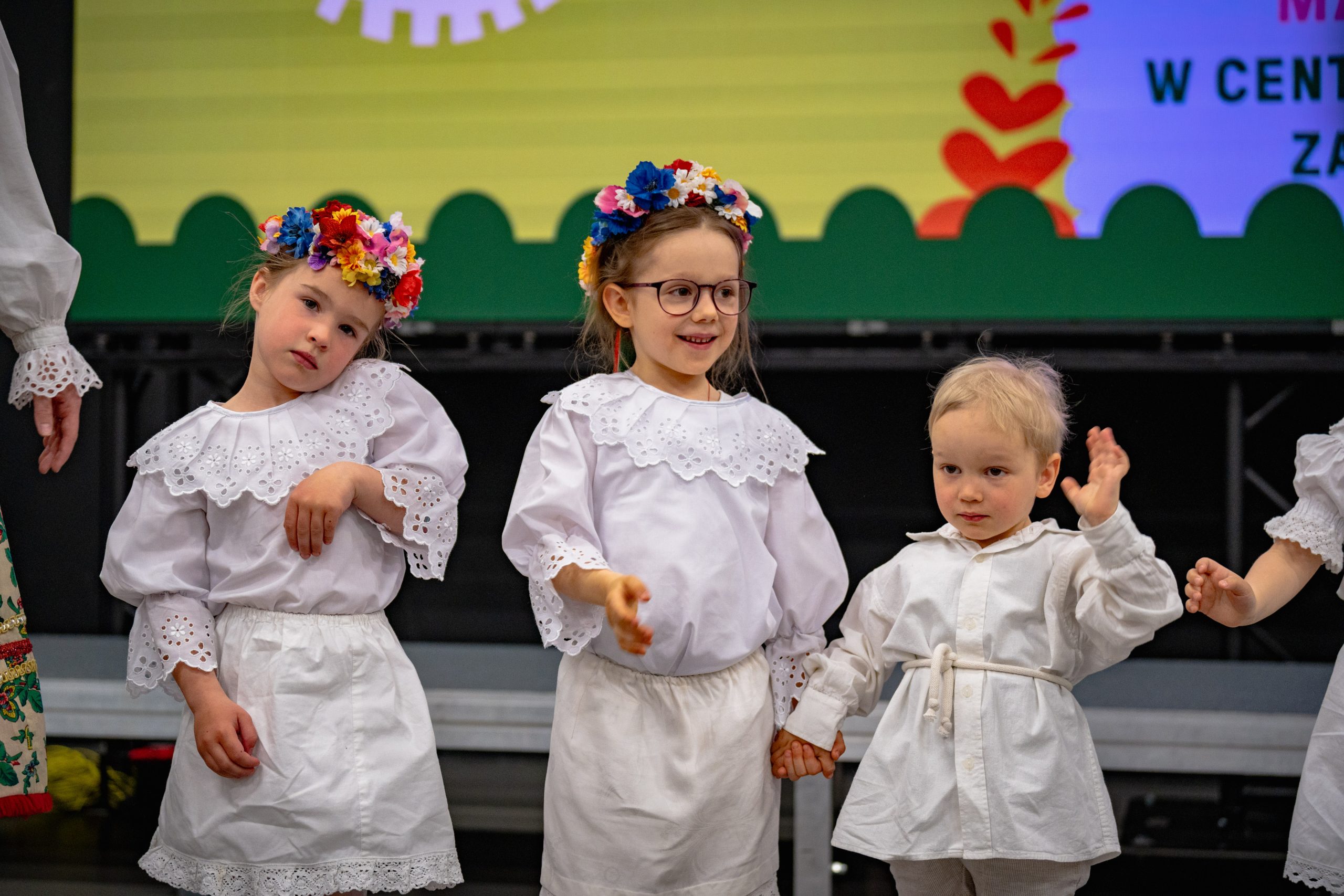 dzieci z grupy 3-6 lat w białych strojach stoją w linii i gestykulują do piosenki
