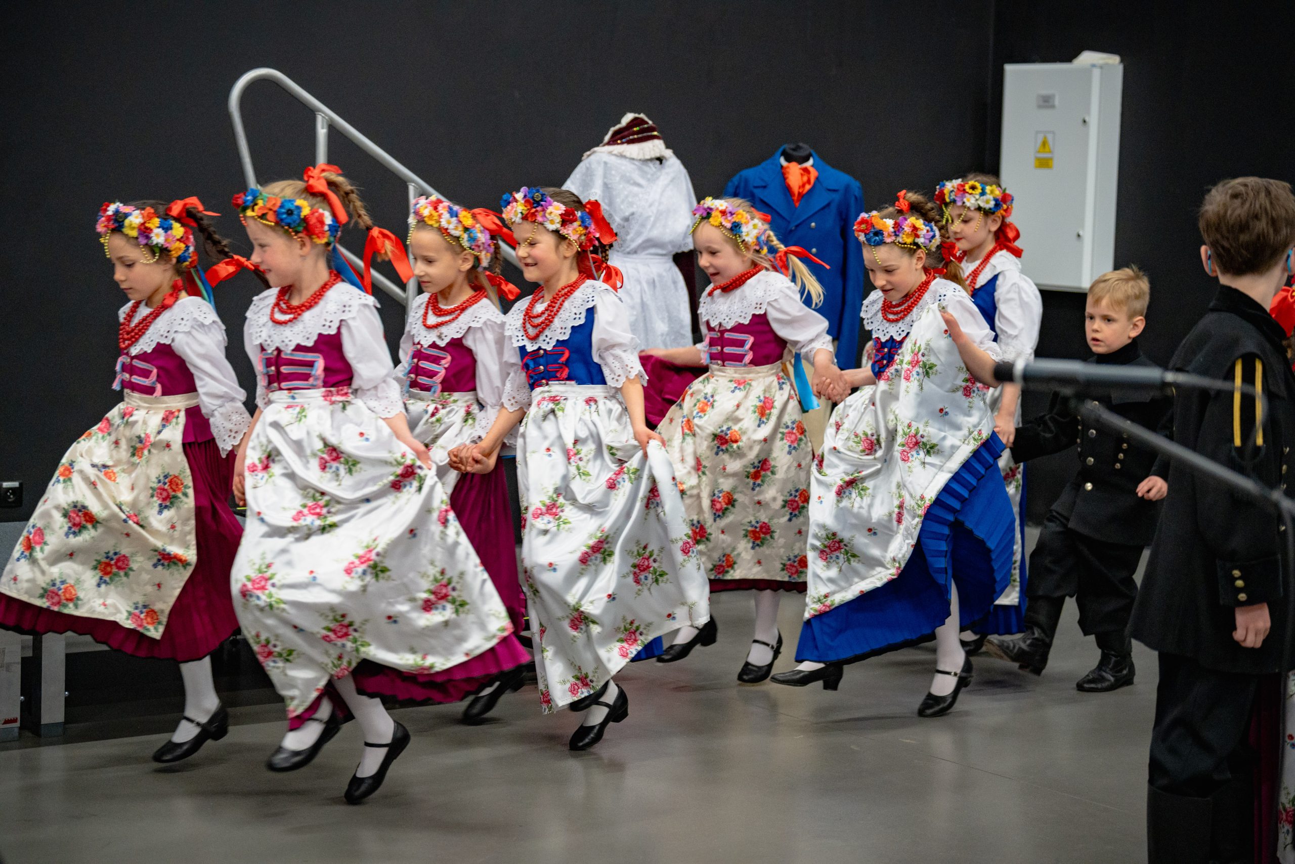 dziewczynki w strojach górnośląskich tańczą krok polki trzymając się w parach za ręce