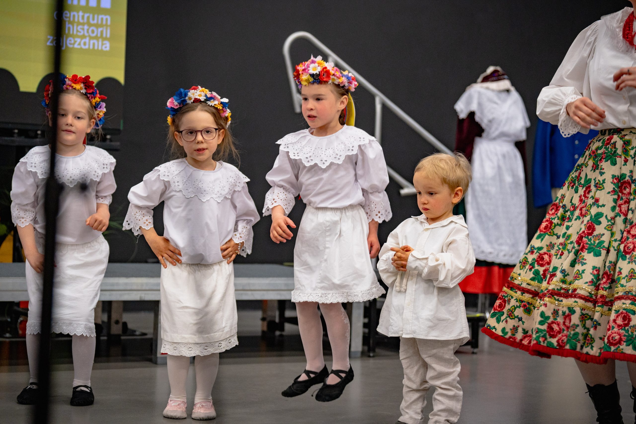 dzieci 3-6 lat w białych strojach stoją w trójce i gestykulują do piosenki
