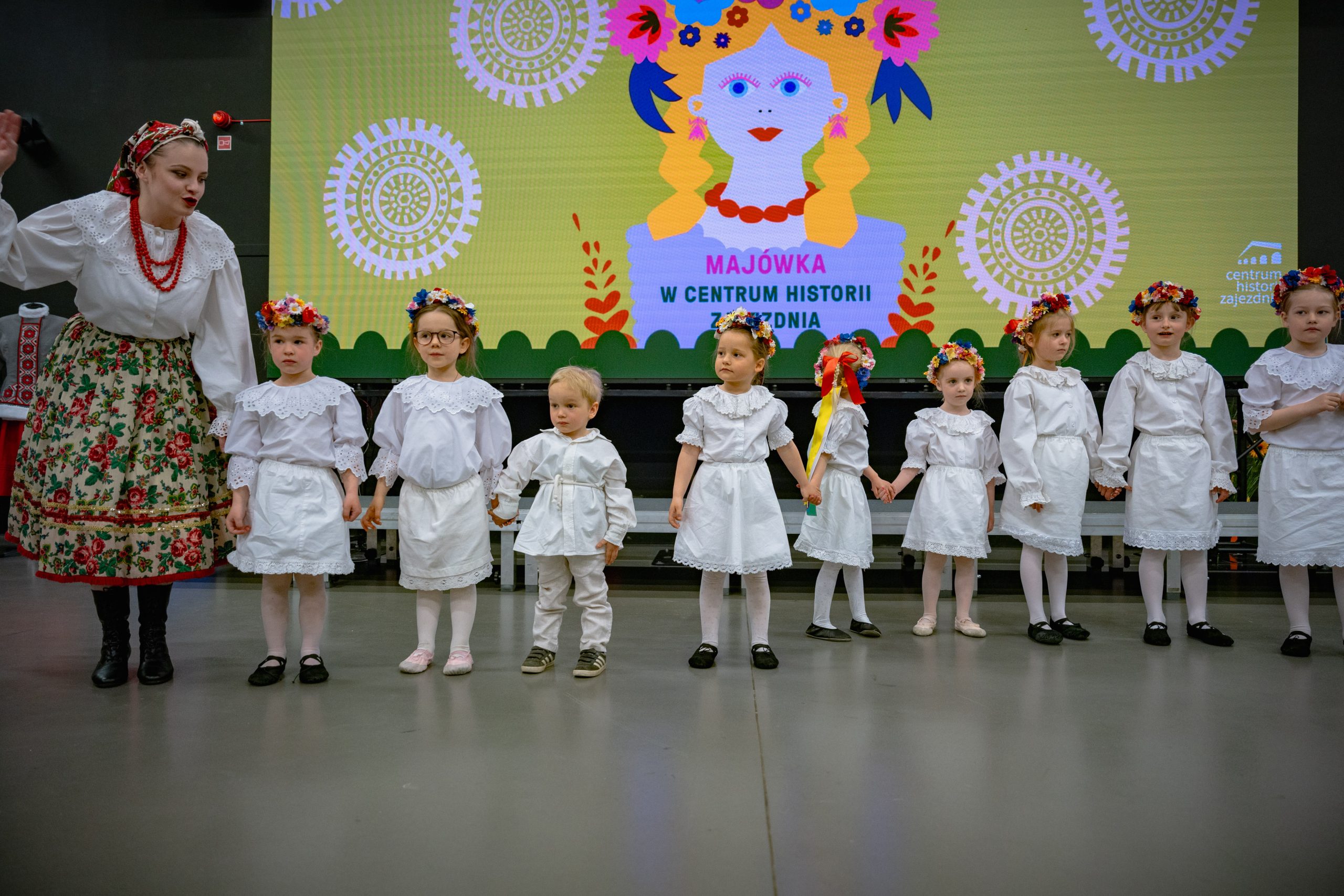 dzieci z grupy 3-6 lat w białych strojach stoją w linii i gestykulują do piosenki