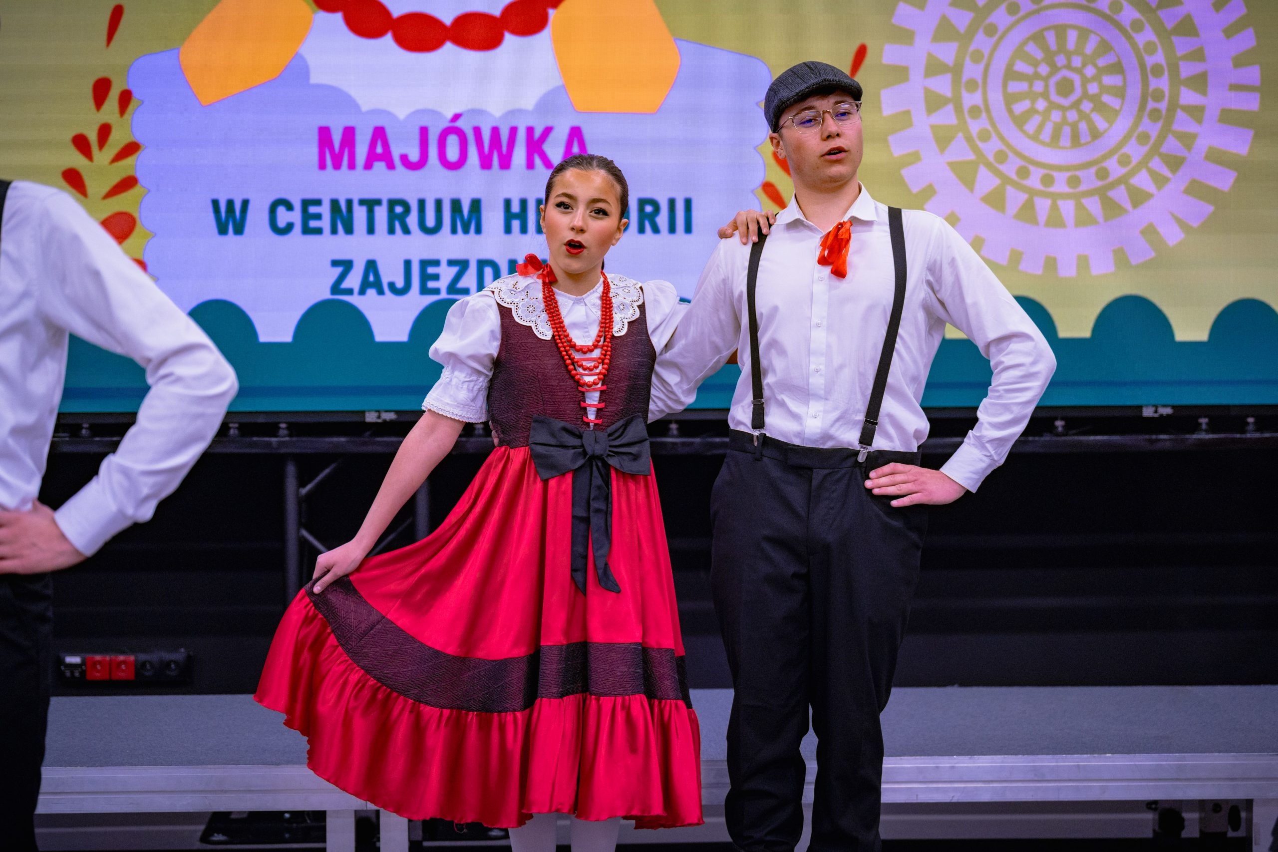 nastolatki w czerwono-czarnych sukienkach oraz chłopcy w białych koszulach, szelkach, czarnych spodniach i kaszkietach w tańcach warszawskich